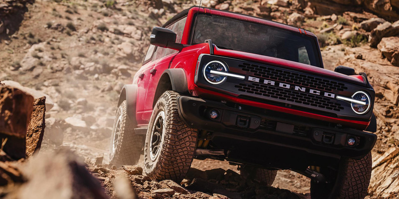 A red Ford Bronco climbing a rocky terrain.