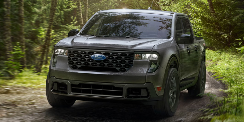 Gray Ford pickup truck driving on a forest trail surrounded by trees, showcasing its rugged exterior design and off-road capability.