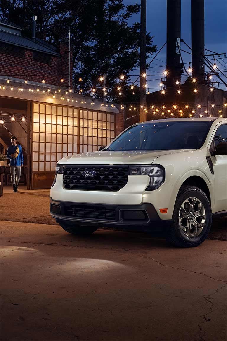 A white Ford Maverick® pickup parked in the forecourt of a restaurant at night.
